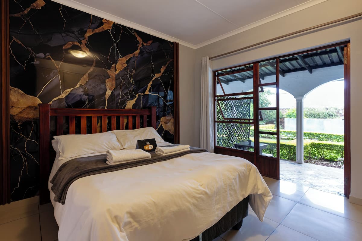Une chambre à coucher avec un lit, un mur en marbre et une vue sur un jardin, visible à travers une porte vitrée.