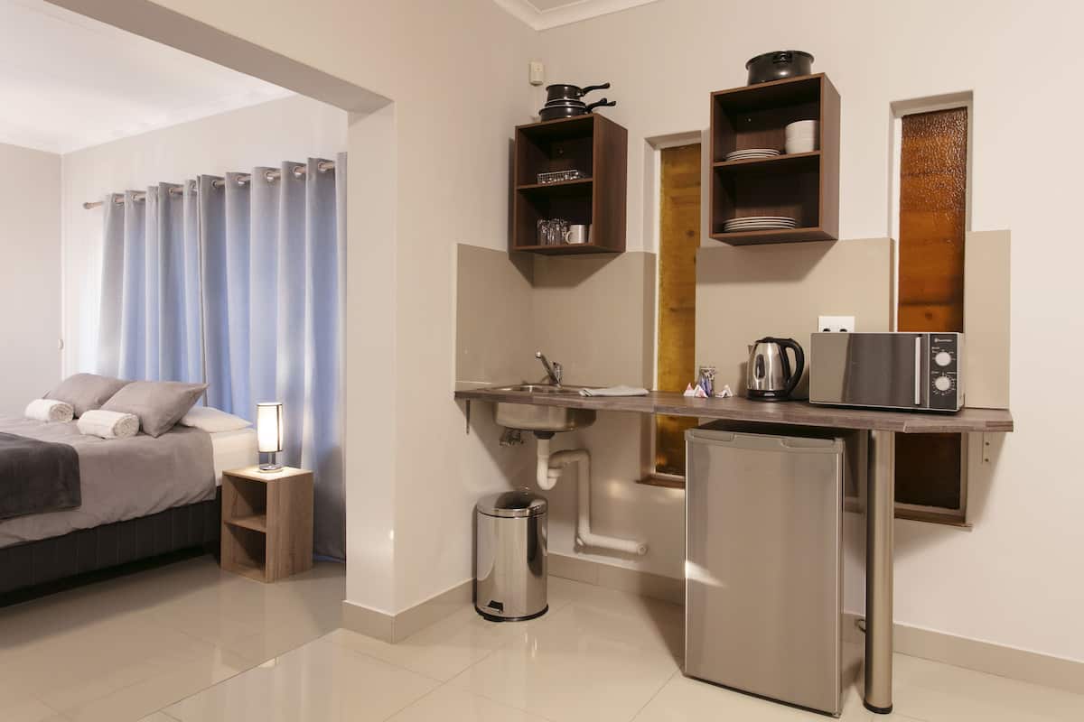 Une chambre d’hôtel moderne équipée d’un lit, d’une petite table de chevet avec une lampe, d’un coin cuisine compact comprenant un évier, un réfrigérateur et un four à micro-ondes.