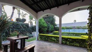 A covered patio with a stone floor, wooden benches, and a view of a well-maintained garden.