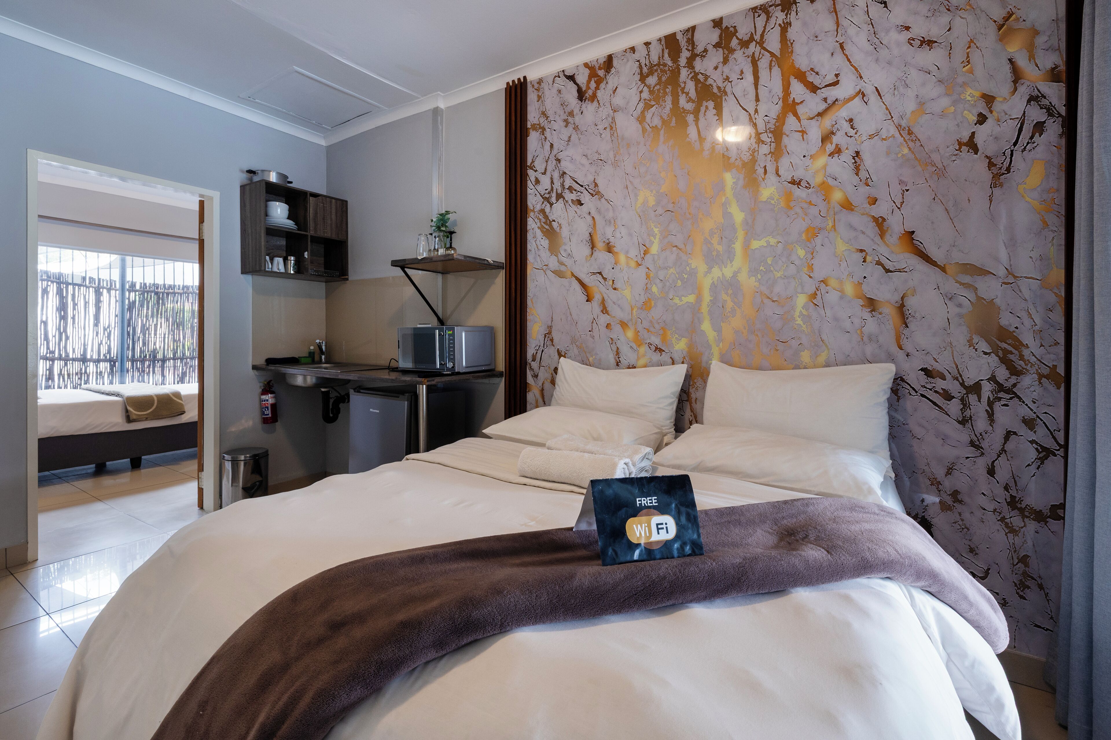 Une chambre d’hôtel avec un lit, un bureau doté d’un micro-ondes, une petite étagère avec quelques objets, et une vue sur l’extérieur.