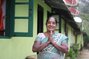 A person standing in front of a green building with a window and a door. - Meena Amma's Tea Experience (Welimada)