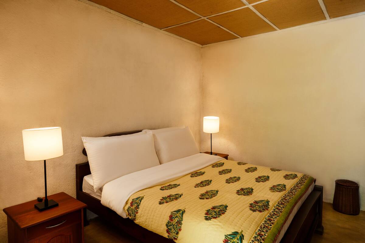 A neatly made bed with a patterned quilt, two bedside lamps, and a small wooden nightstand.