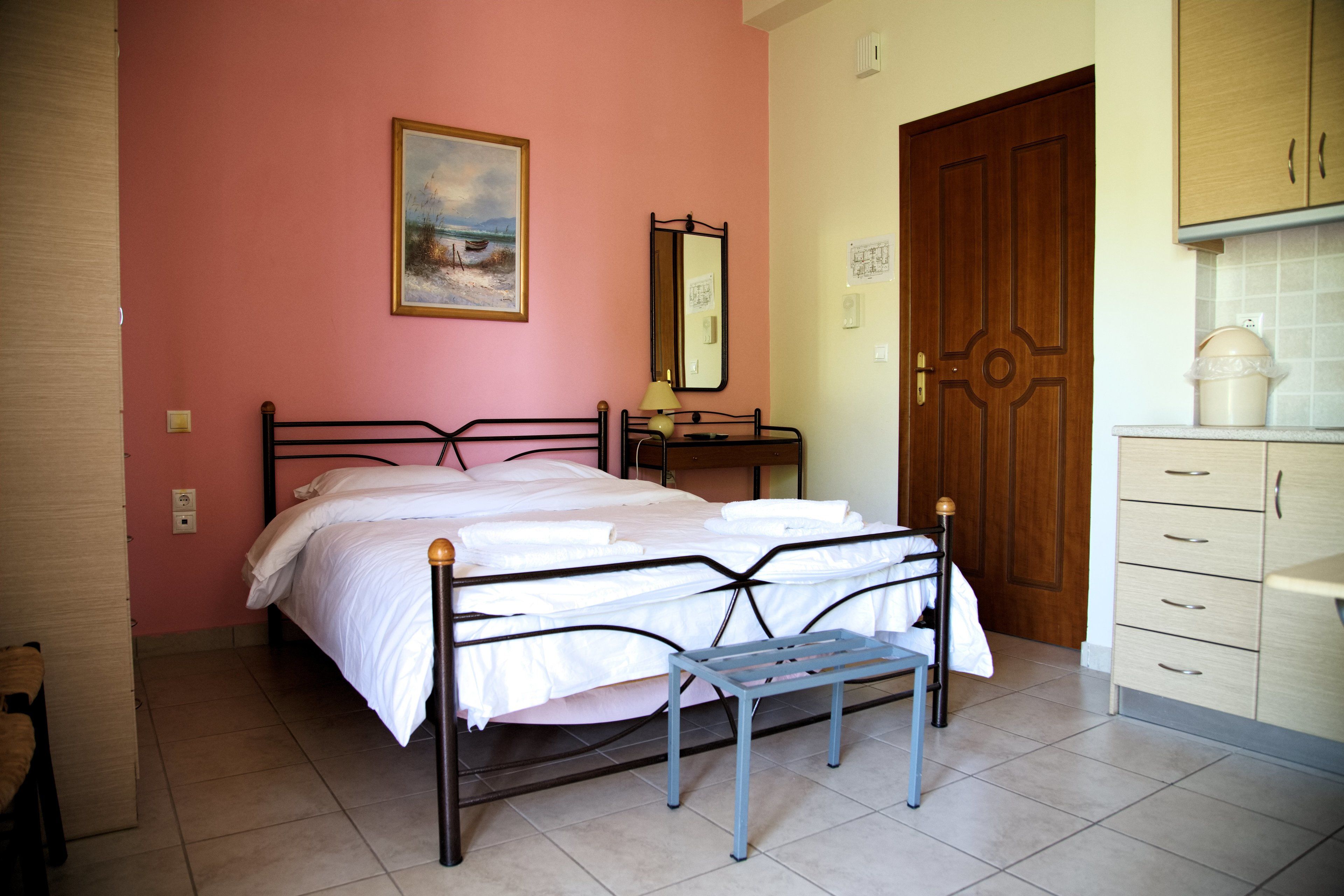 A bedroom with a bed, a bedside table, a mirror, a dresser, and a door.