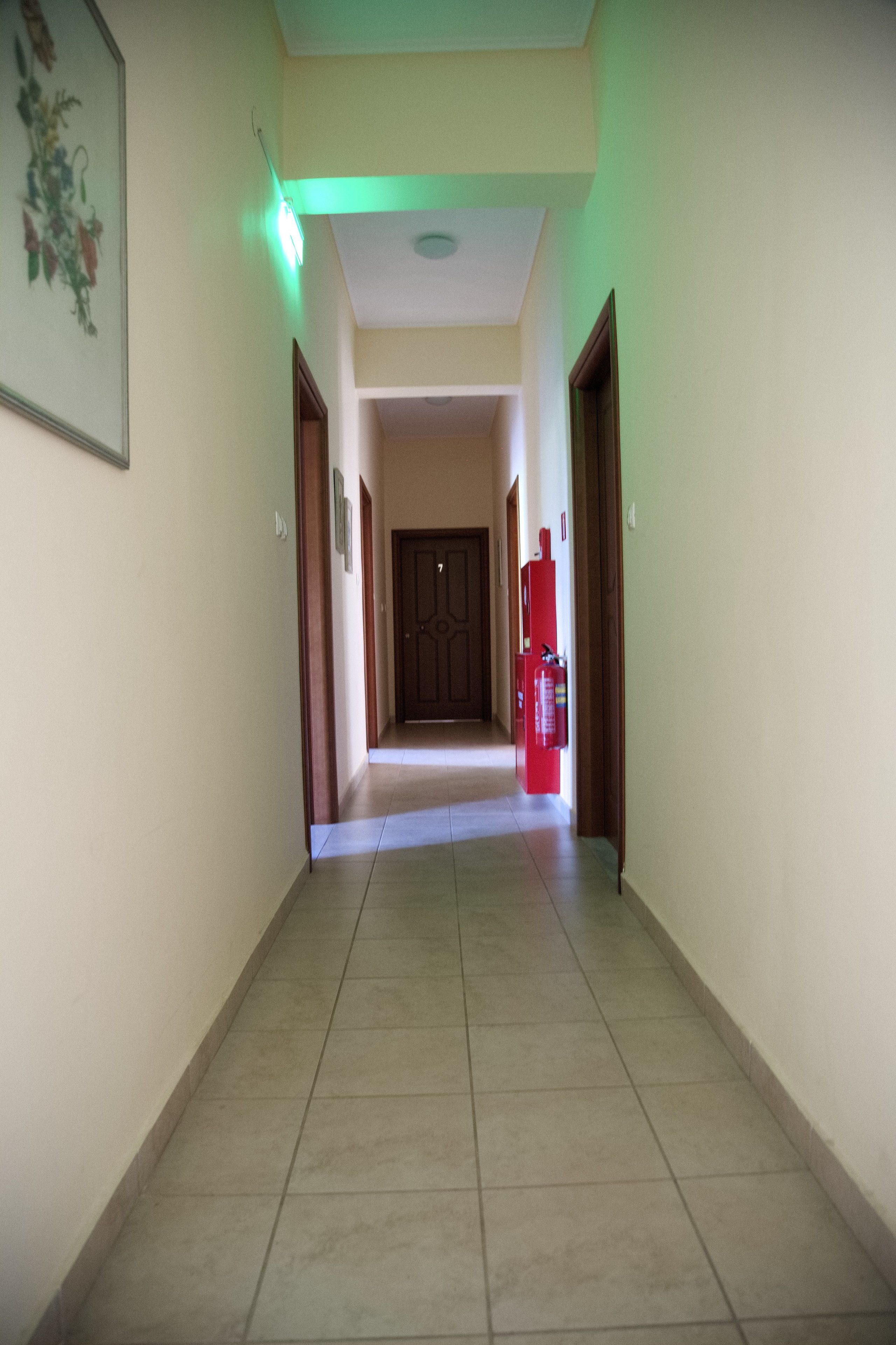Um corredor com chão de azulejos, uma porta no final e um objeto vermelho à direita.