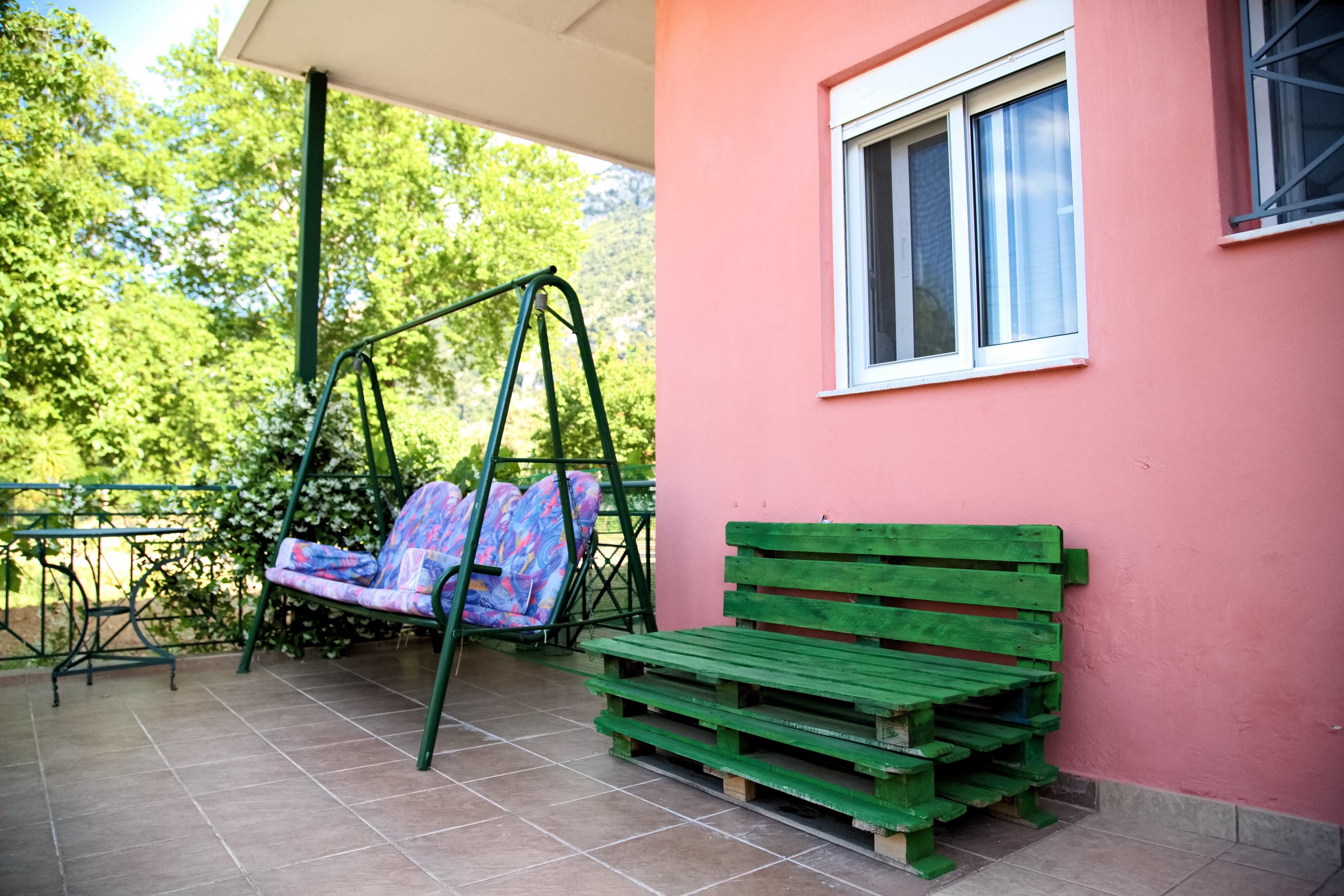 Un patio con una silla colgante, un banco de madera y una ventana.