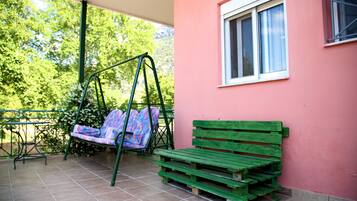 Un patio con una silla colgante, un banco de madera y una ventana.