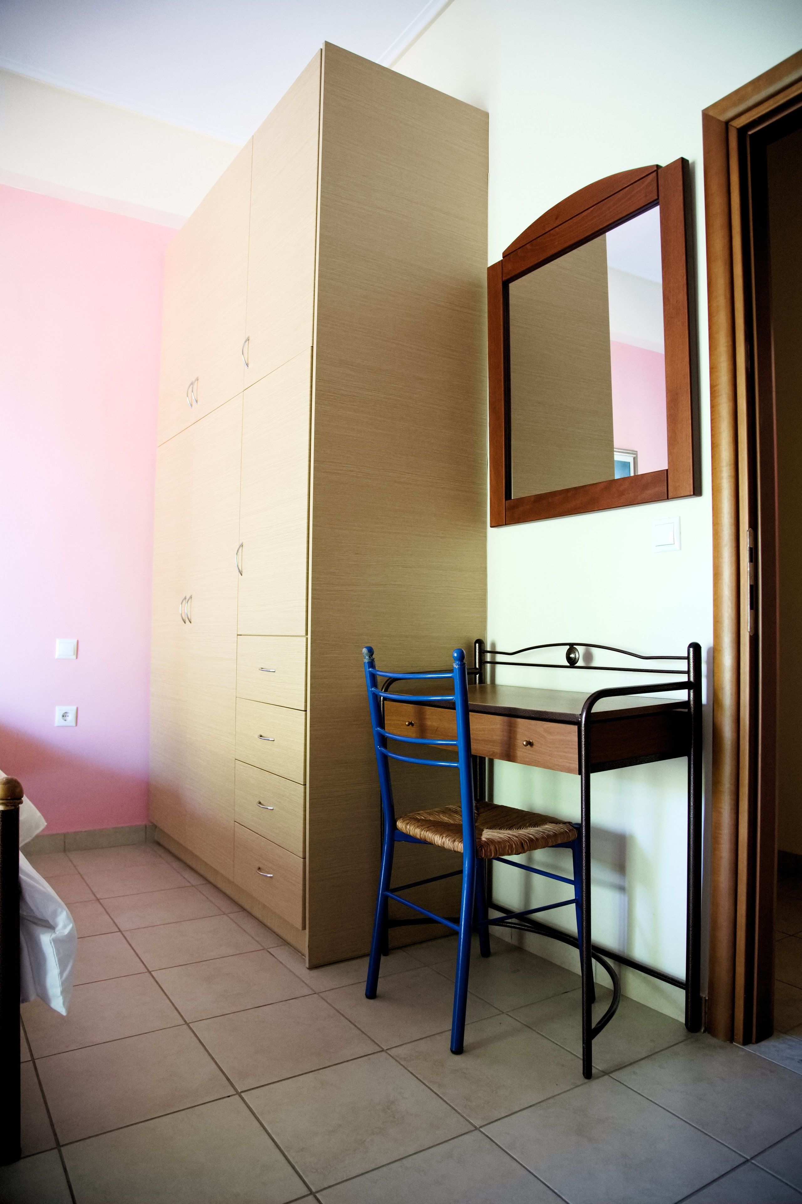 Une chambre avec une armoire en bois, un bureau avec une chaise et un miroir.