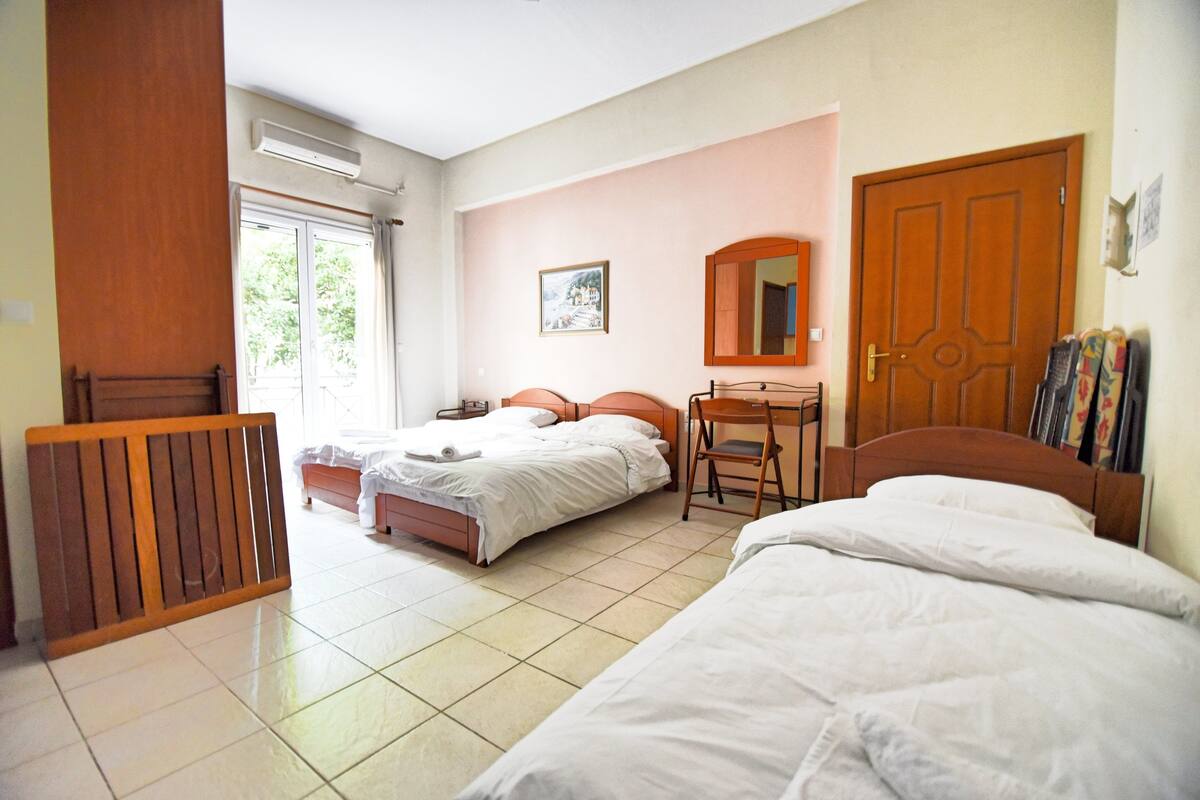 Een hotelkamer met twee bedden, een houten bureau, een stoel, een spiegel en een raam met gordijnen.