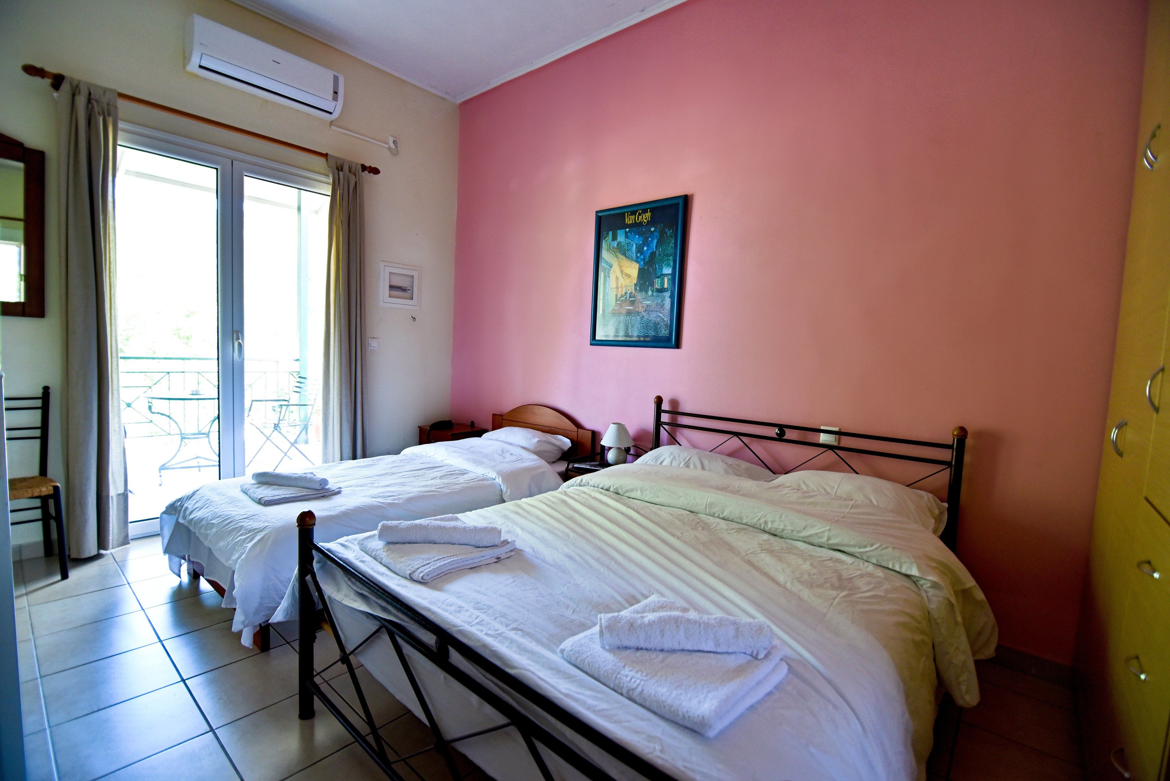 A hotel room with two beds, a balcony, and a painting on the wall.