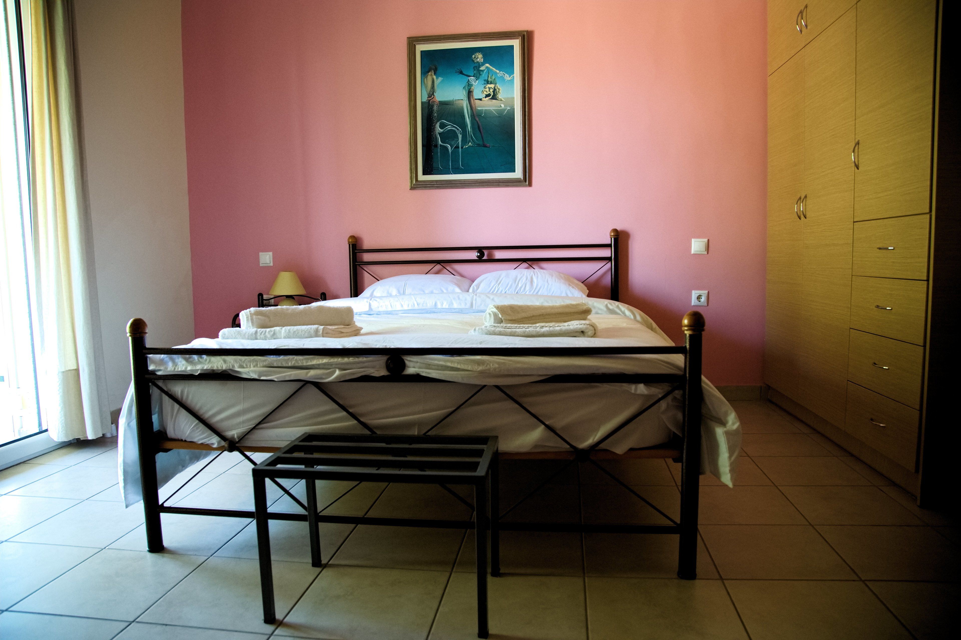 Un llit ben fet a una habitació amb una paret rosa, un armari de fusta i un quadre al capdamunt del llit.
