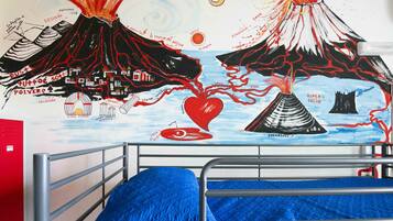 A bedroom with a metal bunk bed, a blue blanket, and a wall mural depicting volcanoes and a heart.