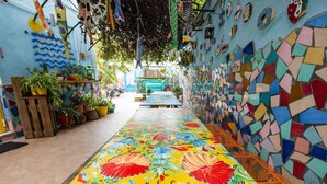 A narrow corridor with colorful mosaic walls, potted plants, and a vibrant floral-patterned floor. - Eco Hostel Floreale (Ercolano)