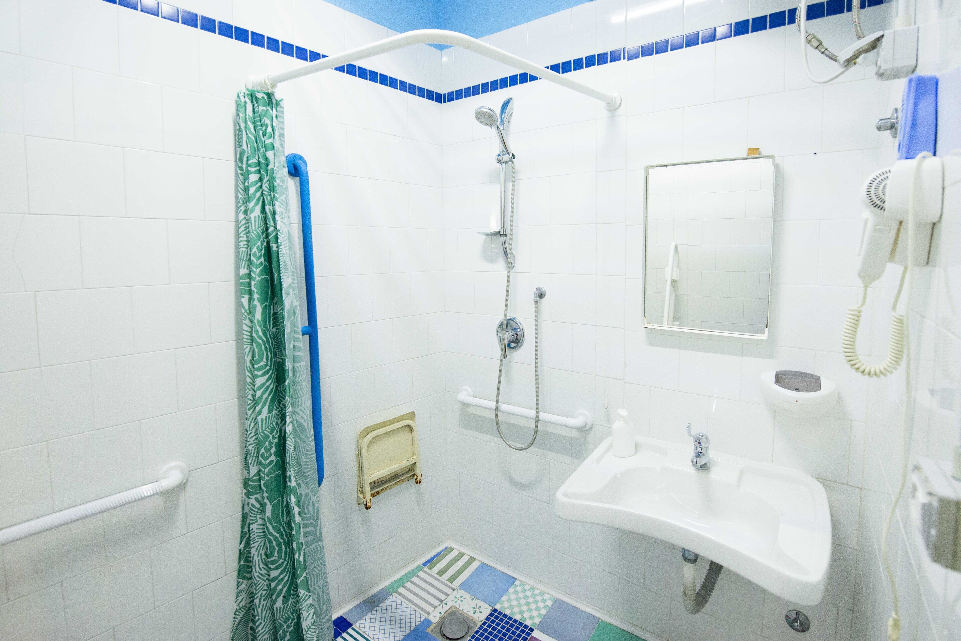 Un baño con ducha, lavamanos, espejo y teléfono.