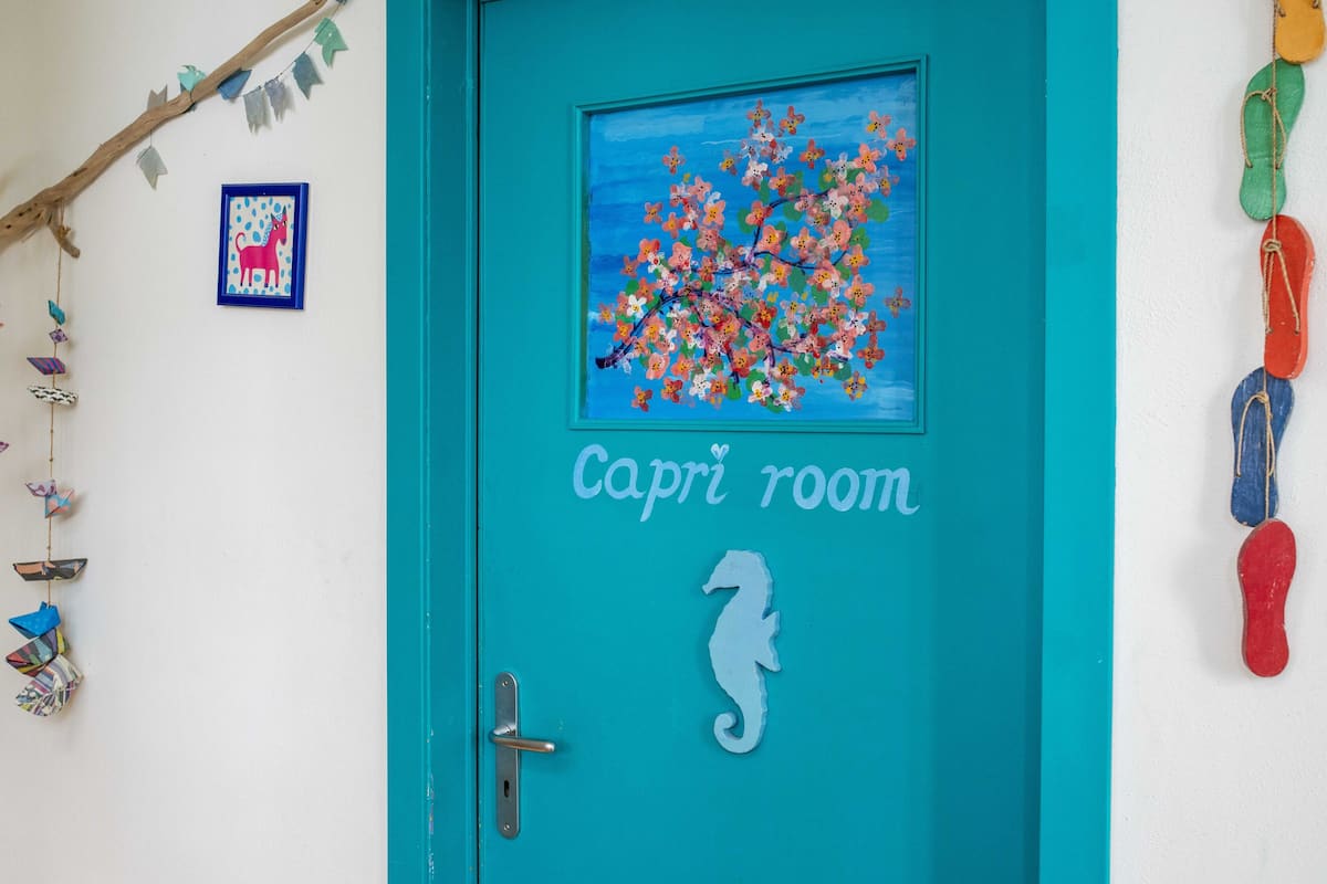 Una puerta turquesa con un adhesivo de caballito de mar y una pintura de un árbol con flores coloridas.
