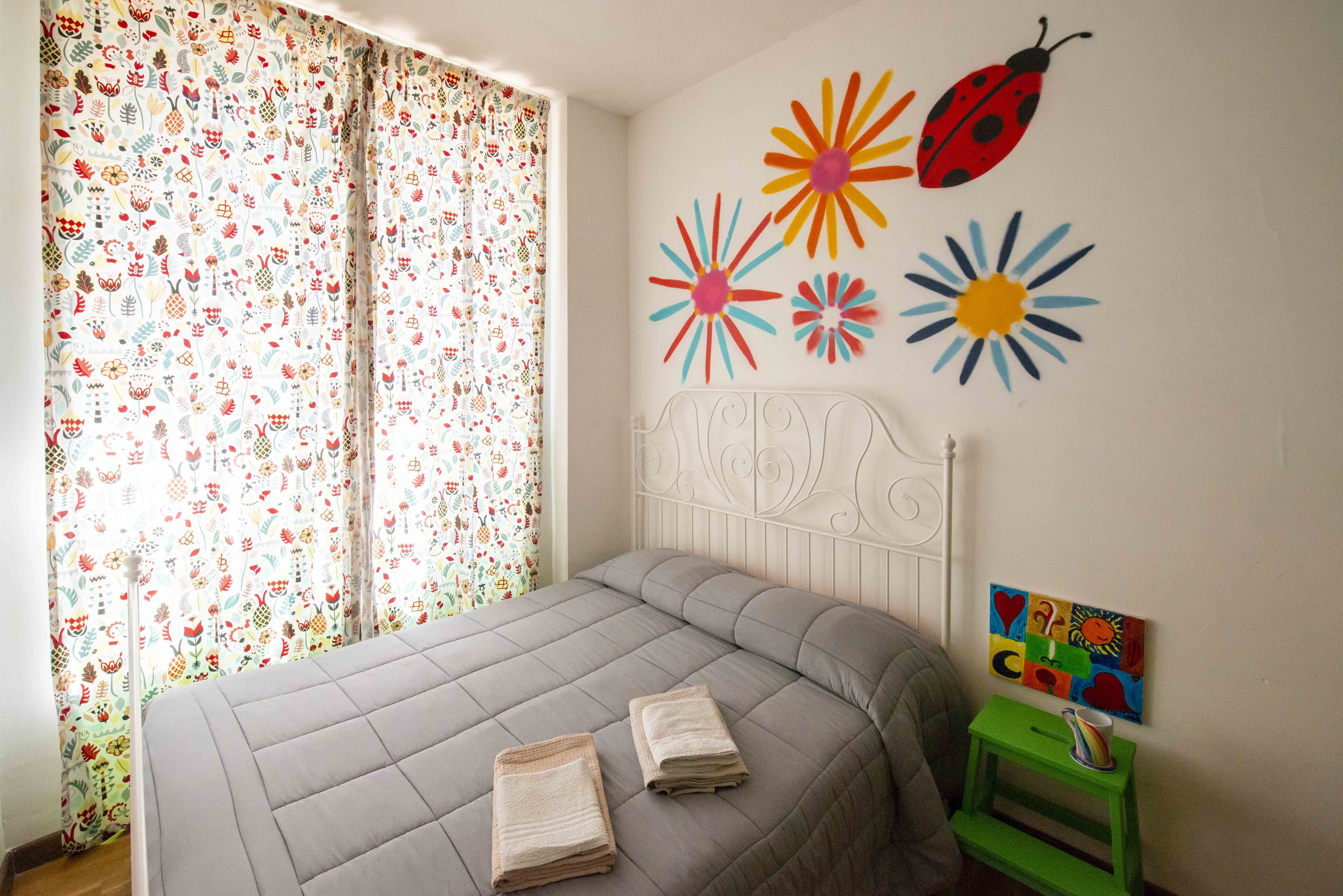 Un dormitorio con cama, cortinas, decoración en la pared y una mesita.