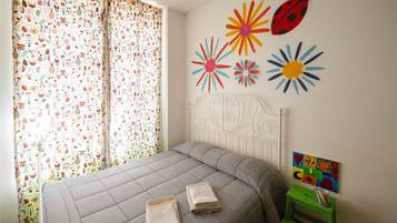 Un dormitorio con cama, cortinas, decoración en la pared y una mesita.
