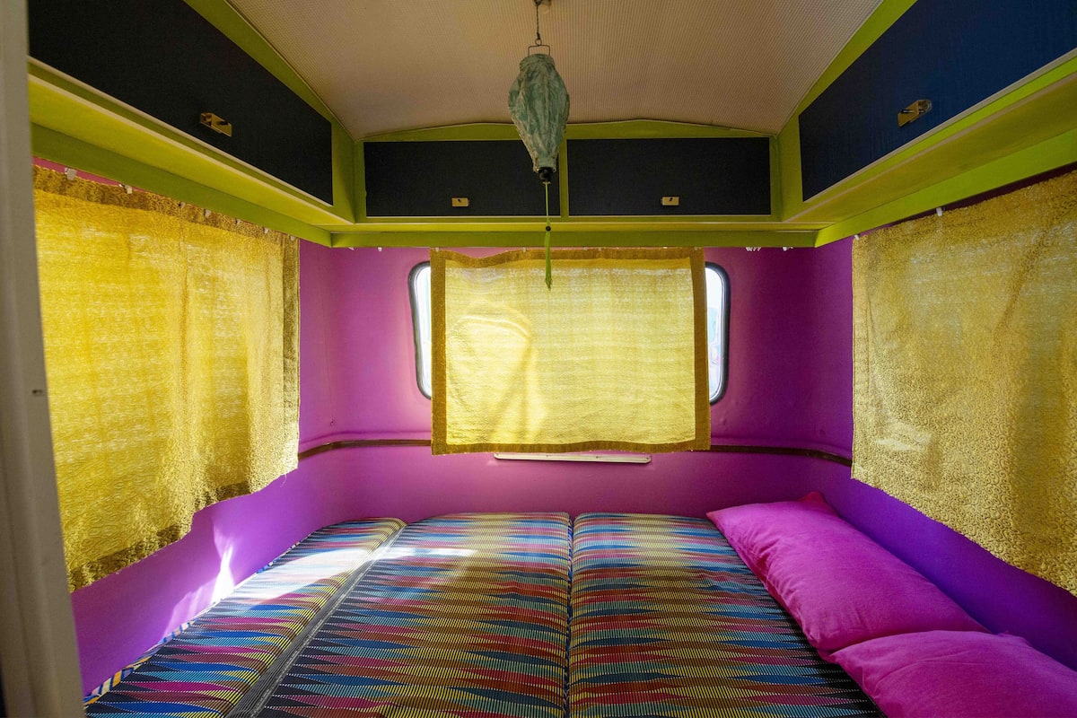Una habitación pequeña y de colores vivos con una cama, una ventana y una lámpara colgante.