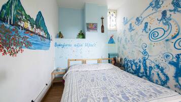 Un dormitorio con cama, un mural en la pared y una mesita con una botella y una planta.