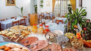 Un espace repas avec plusieurs tables préparées pour le petit-déjeuner, où l’on propose une variété de viennoiseries, de sandwichs et de boissons.