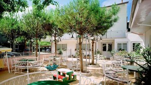 Un espace extérieur aménagé en terrasse, avec des tables et des chaises rondes, entouré d’arbres et de plantes en pot.