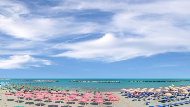 Une plage avec de nombreux parasols et des chaises longues, un ciel dégagé et une mer calme.
