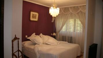 A bedroom with a bed, a chandelier, a window with curtains, and a picture on the wall.
