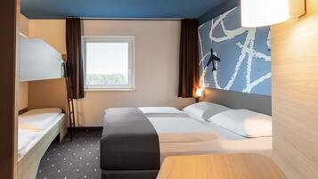 Ein Hotelzimmer mit Etagenbett, einem Einzelbett, einem Schreibtisch und einem großen Fenster.