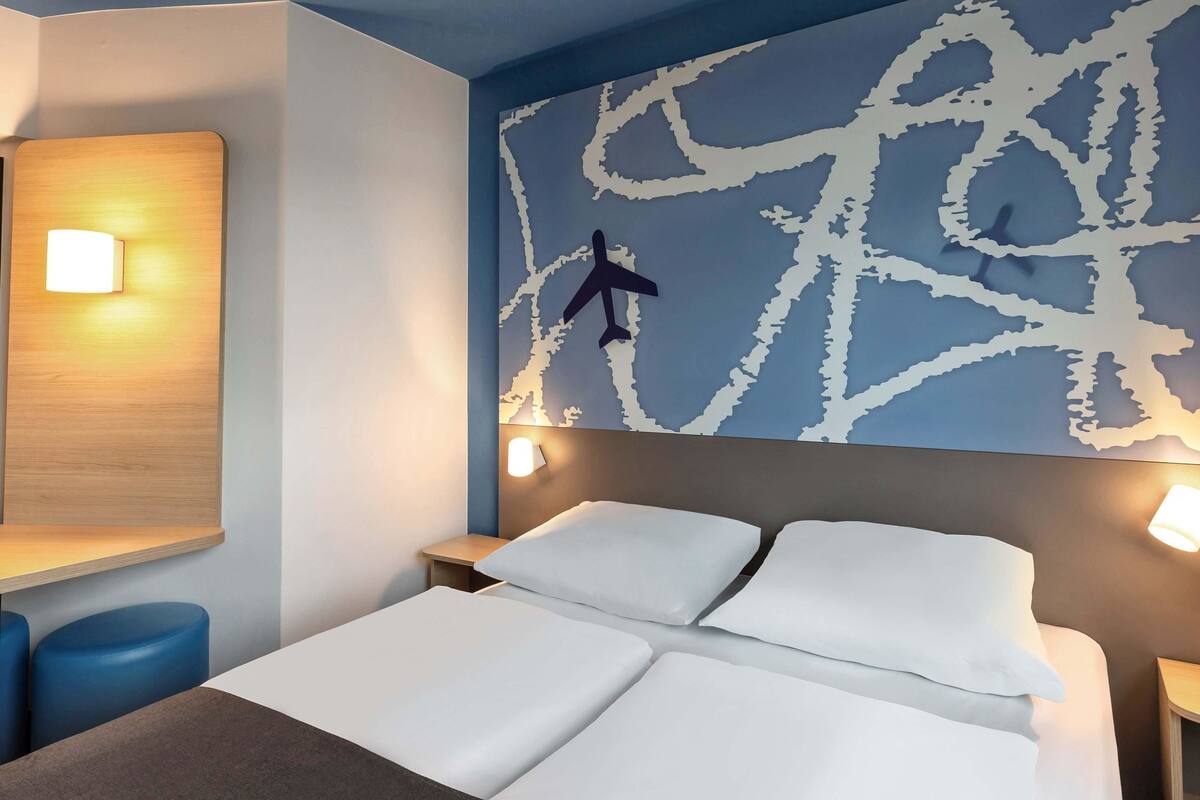 A hotel room with a bed, two bedside tables, a nightstand, and a wall with a map design.