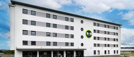 Un hotel B&B moderno con fachada blanca, varios pisos y un estacionamiento al frente.