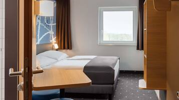 Ein Hotelzimmer mit Bett, Schreibtisch, Stuhl, Fenster und Vorhang.