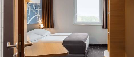 A hotel room with a bed, a desk, a chair, a window, and a curtain.