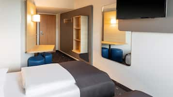 Et hotelværelse med seng, skrivebord, stol, fjernsyn og spejl.