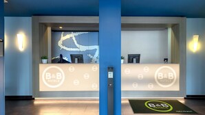 A reception area with a blue wall, a reception desk, and a digital screen. - B&B Hotel Frankfurt-Hahn Airport (Lautzenhausen)