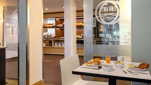 A breakfast area with a table set for two, including a plate of food, a bowl of cereal, a glass of orange juice, and a muffin. - B&B Hotel Frankfurt-Hahn Airport (Lautzenhausen)