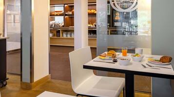 A breakfast area with a table set for two, including a plate of food, a bowl of cereal, a glass of orange juice, and a muffin.