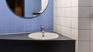 A bathroom with a round mirror, a white sink, and blue and white tiled walls. - B&B Hotel Frankfurt-Hahn Airport (Lautzenhausen)