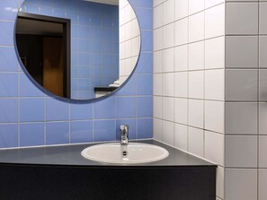 A bathroom with a round mirror, a white sink, and blue and white tiled walls. - B&B Hotel Frankfurt-Hahn Airport (Lautzenhausen)