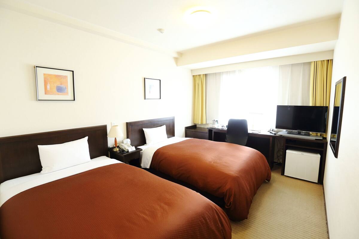 A hotel room with two beds, a desk, a television, and a small refrigerator.