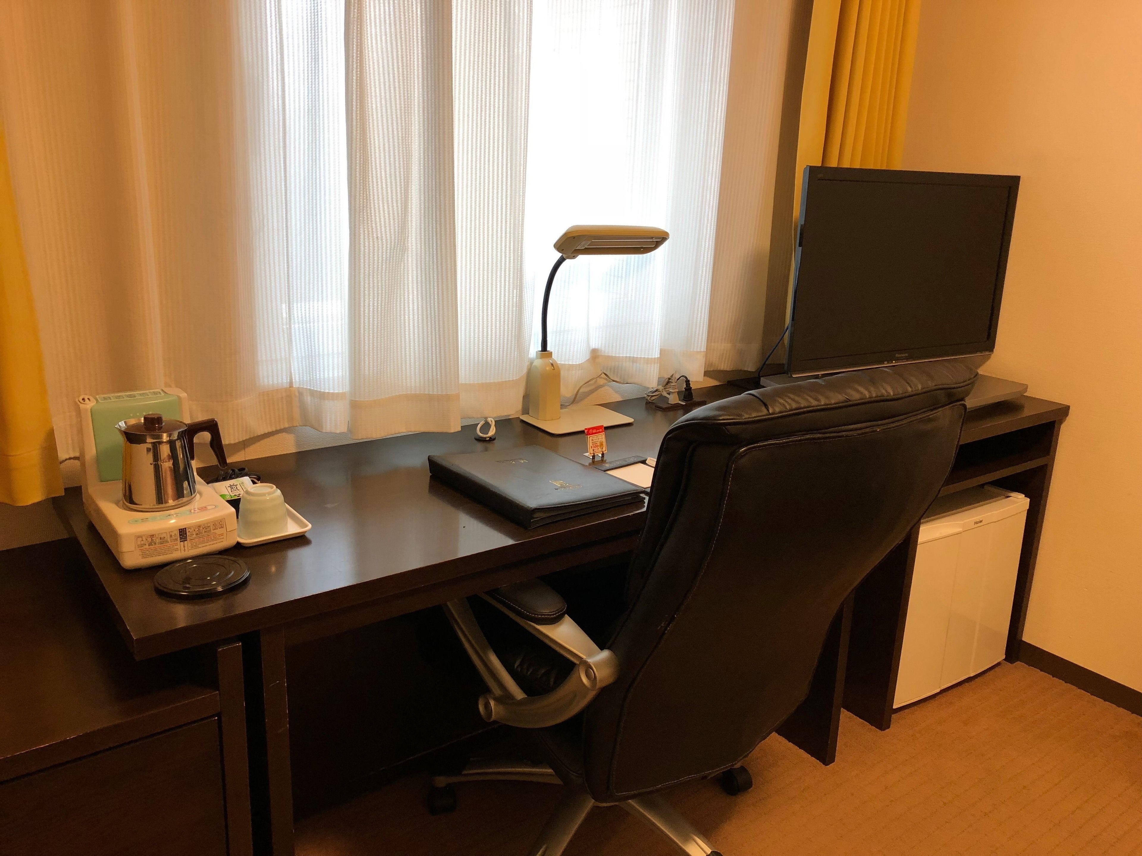 Une chambre d’hôtel équipée d’un bureau, d’une chaise, d’une télévision, d’une machine à café et d’un petit réfrigérateur.