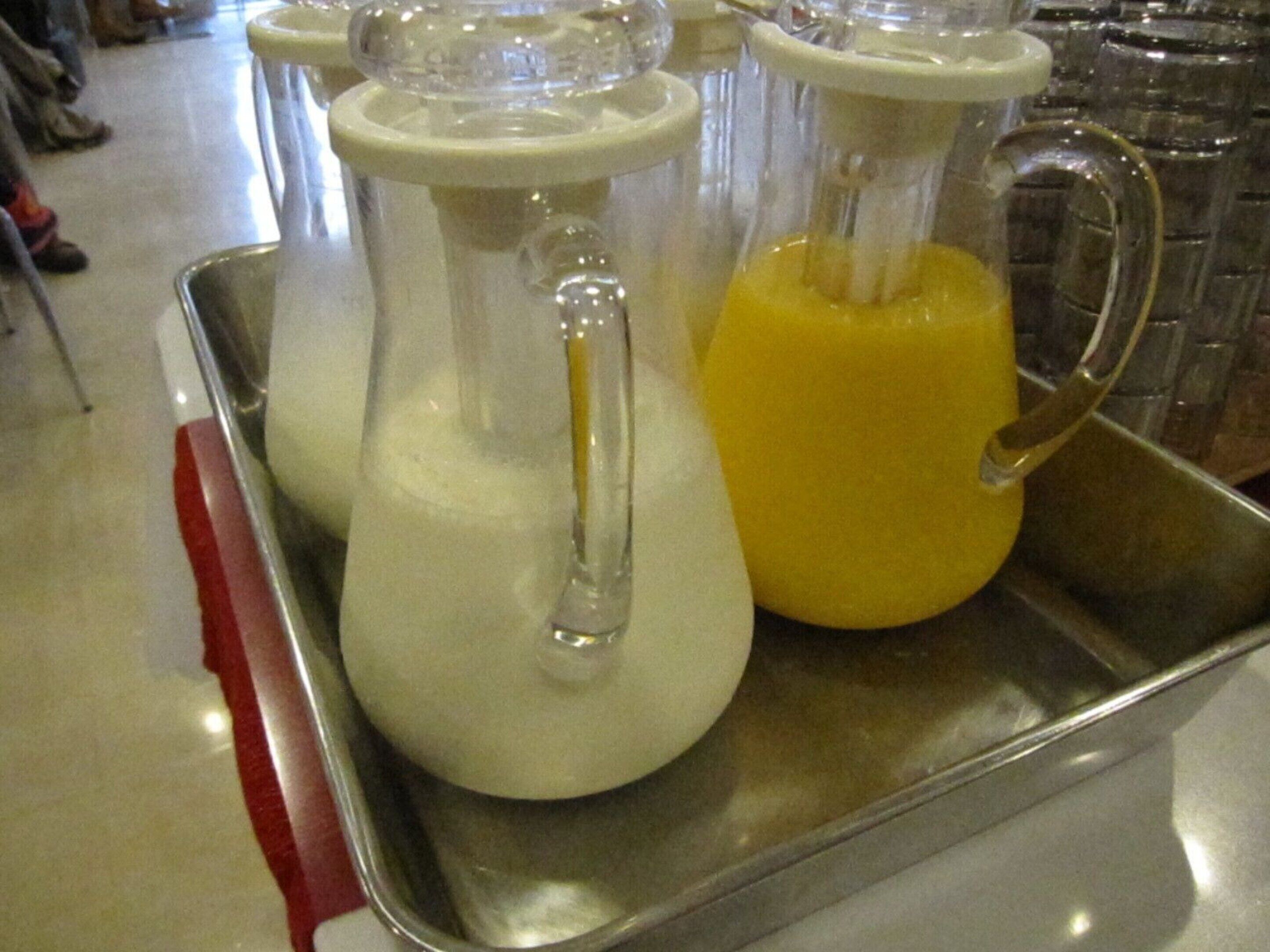 Una bandeja de acero inoxidable con dos recipientes de vidrio, uno con líquido blanco y otro con líquido amarillo.