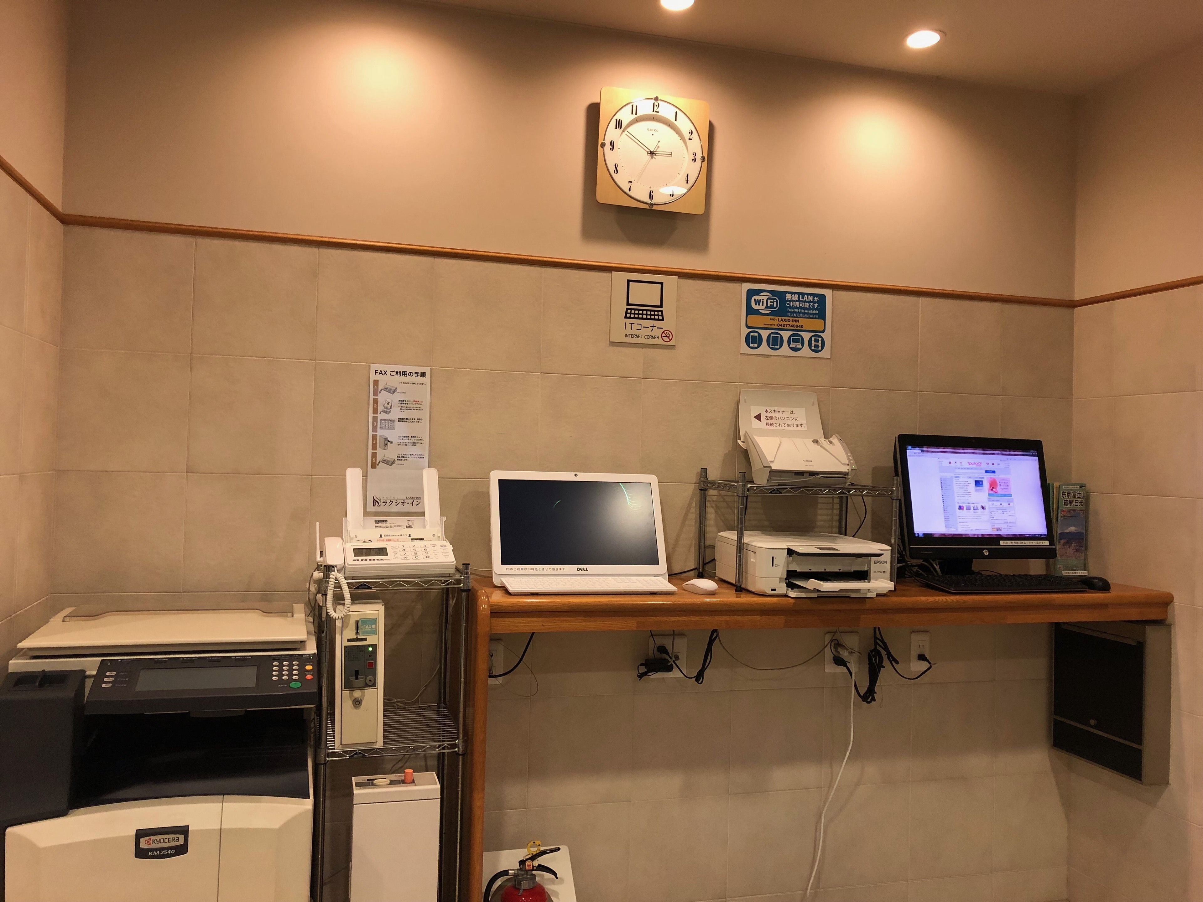 A reception area with a desk, a clock, a fax machine, a laptop, a printer, and a fire extinguisher.