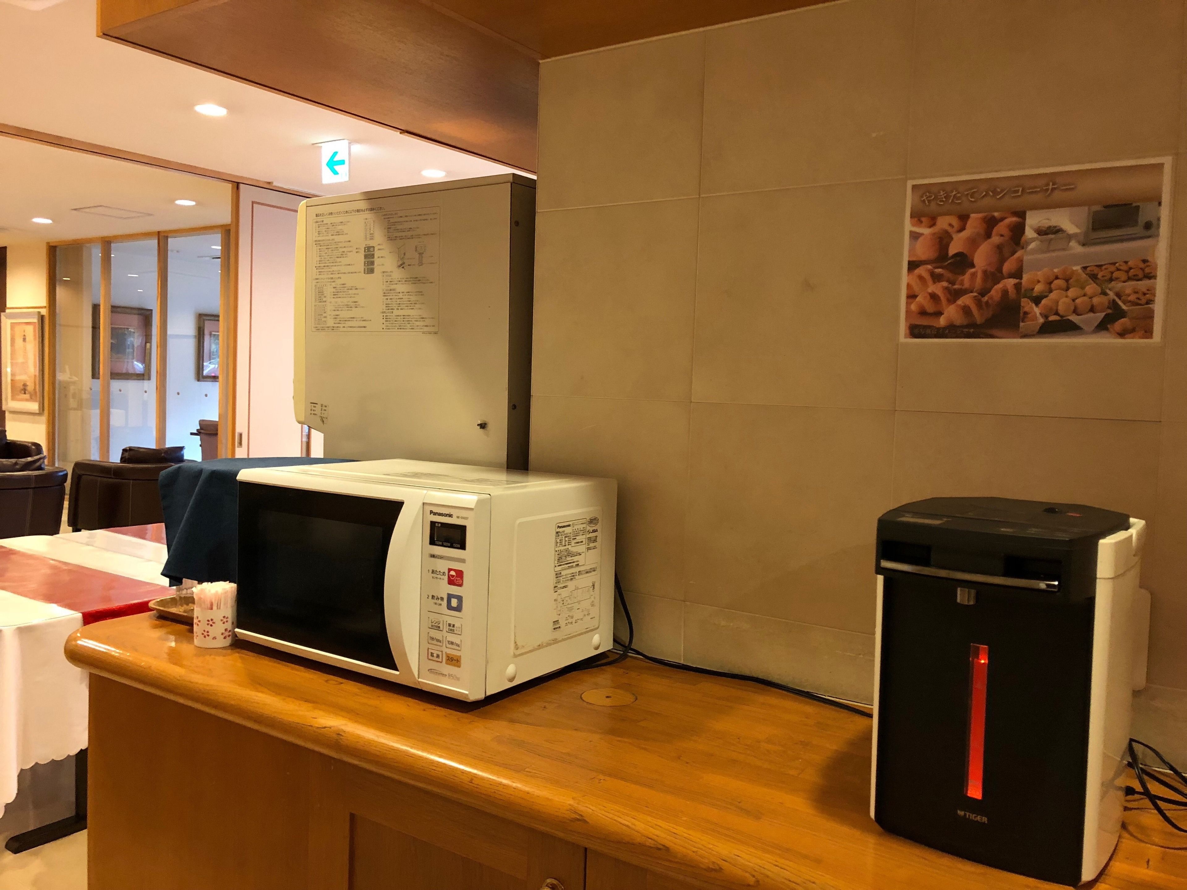 A kitchen area with a microwave, a black coffee machine, and a poster on the wall.