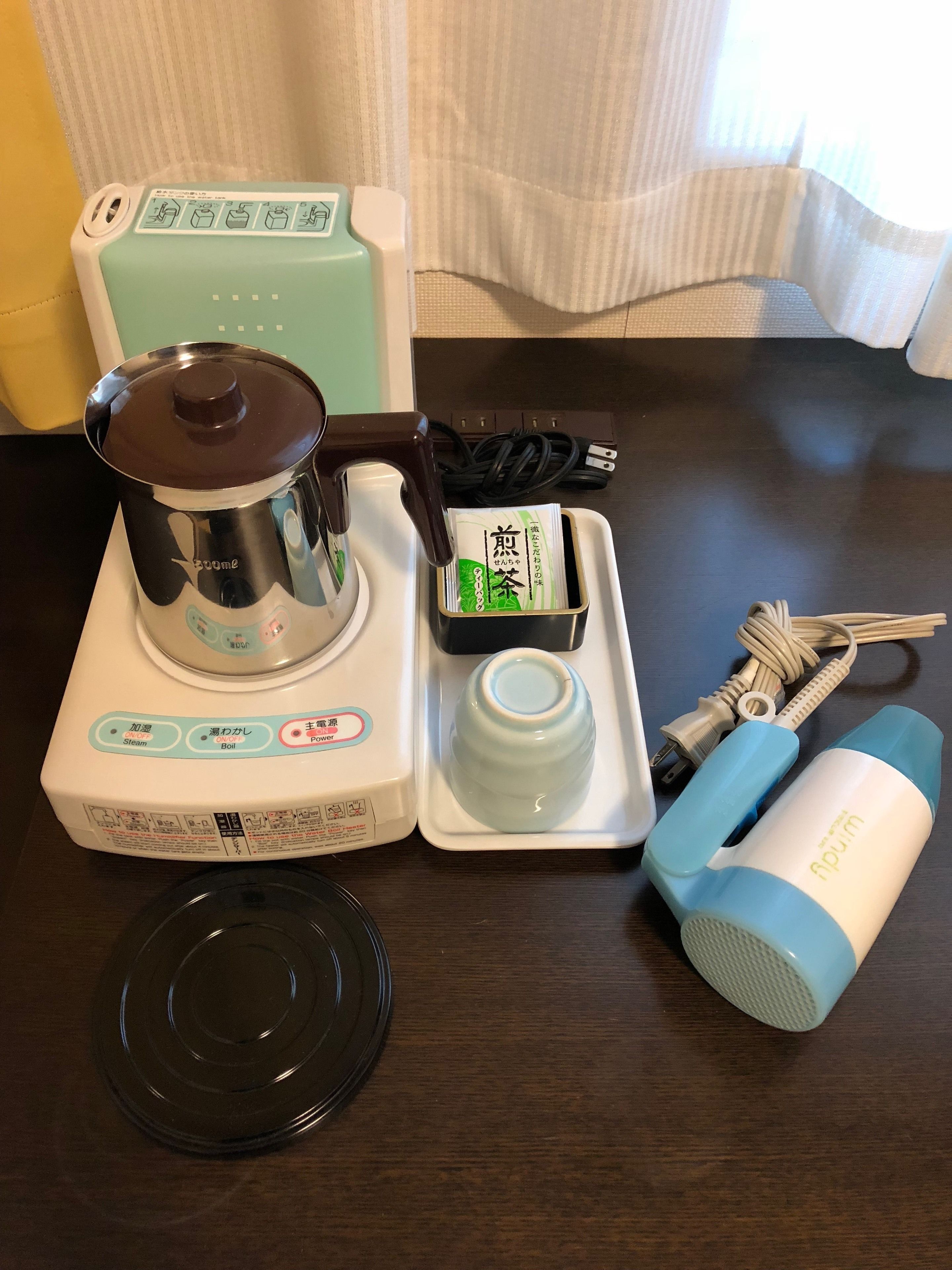 A kitchen setup with a coffee maker, a kettle, a tea kettle, a cup, and a pair of scissors on a wooden table.