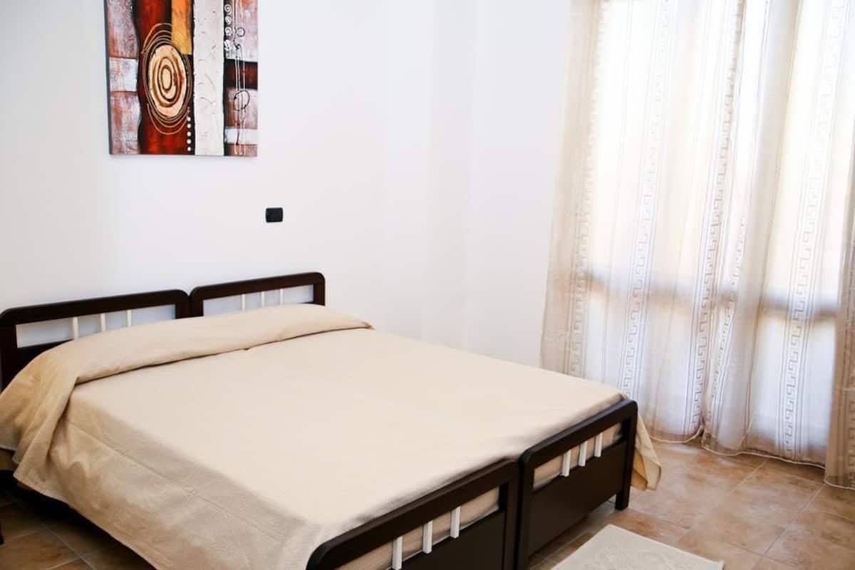 Um quarto com uma cama, uma obra de arte na parede e uma janela com cortinas.