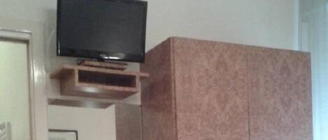 A bedroom with a bed, a wardrobe, a television, and a small enclosed space with a picture frame.