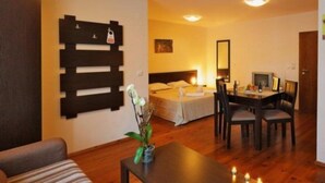 A hotel room with a bed, bedside table, and a desk with chairs. There is a wooden wall decoration and a small plant on the desk. - Grand Montana (Bansko)