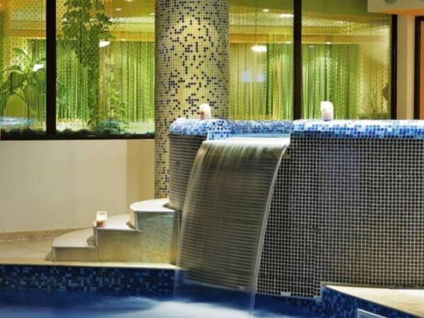 A hot tub with a tiled waterfall feature, surrounded by a tiled wall with a mosaic pattern.