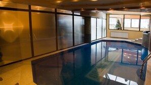 A modern indoor pool area with glass walls, a clear pool, and a view of the outside. - Grand Montana (Bansko)