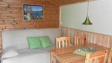 A wooden cabin interior with a wooden table and chairs, a green cushion on a sofa, and a picture on the wall.