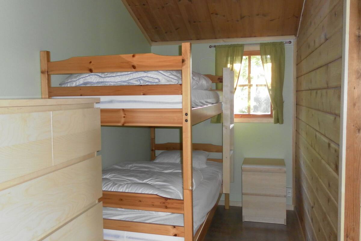 A bunk bed room with a wooden headboard, a window with green curtains, and a small wooden dresser.